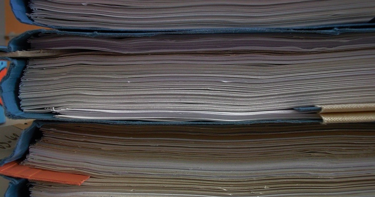 Detalle lateral de expedientes y carpetas con documentos Vista lateral de expedientes apilados con hojas y carpetas azules, sin datos legibles